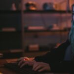 Kobieta o niebieskich włosach pracuje przy komputerze w ciemnym pokoju cyber