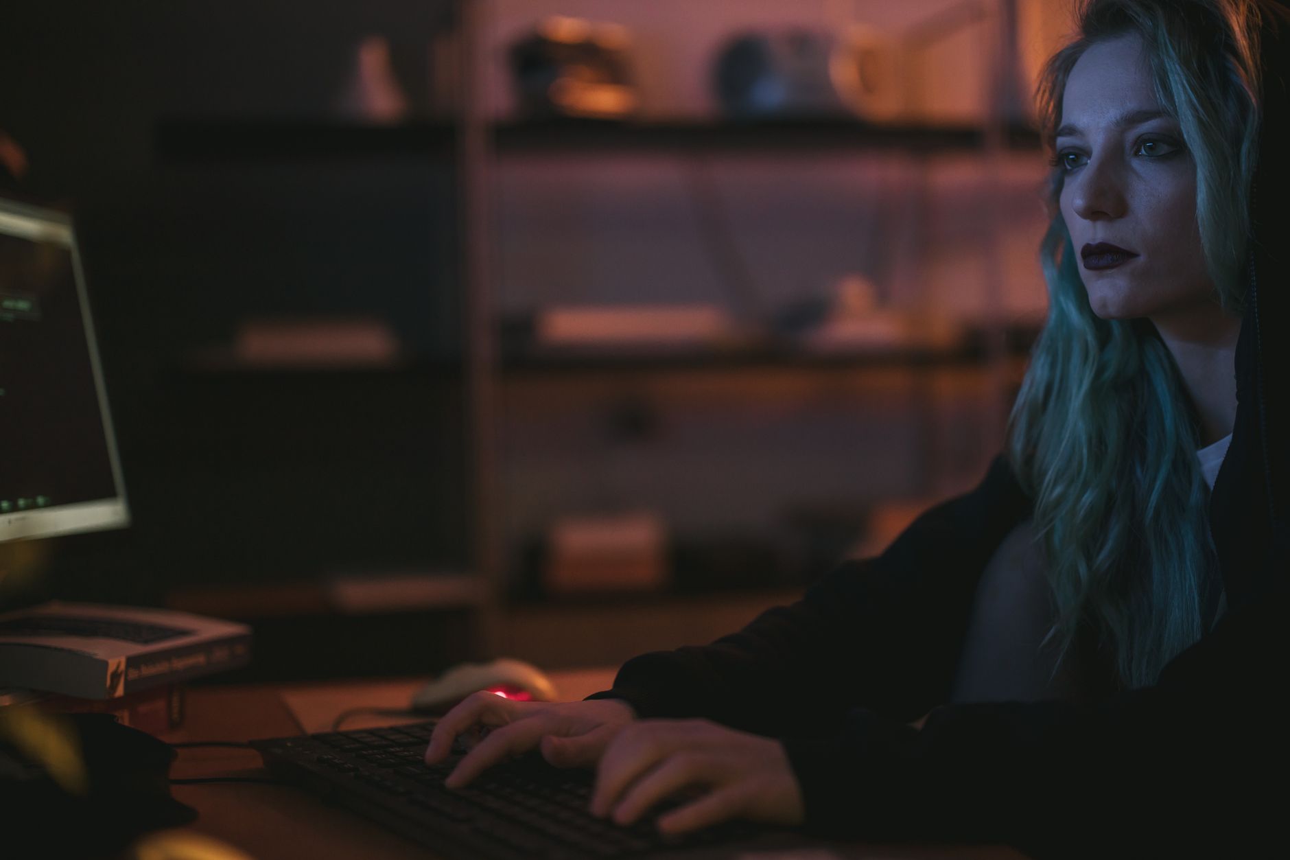 Kobieta o niebieskich włosach pracuje przy komputerze w ciemnym pokoju cyber