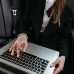 Kobieta w czarnej marynarce pracuje na laptopie w samochodzie