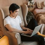 Mężczyzna siedzący w fotelu i korzystający z laptopa w salonie