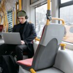 Ochrona w podróży jak zabezpieczyć telefon i laptop w hotelu na lotnisku i w kawiarni Mężczyzna w czarnym płaszczu pracuje na laptopie w tramwaju