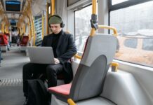 Ochrona w podróży jak zabezpieczyć telefon i laptop w hotelu na lotnisku i w kawiarni Mężczyzna w czarnym płaszczu pracuje na laptopie w tramwaju