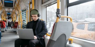 Ochrona w podróży jak zabezpieczyć telefon i laptop w hotelu na lotnisku i w kawiarni Mężczyzna w czarnym płaszczu pracuje na laptopie w tramwaju