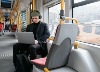 Ochrona w podróży jak zabezpieczyć telefon i laptop w hotelu na lotnisku i w kawiarni Mężczyzna w czarnym płaszczu pracuje na laptopie w tramwaju