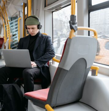 Ochrona w podróży jak zabezpieczyć telefon i laptop w hotelu na lotnisku i w kawiarni Mężczyzna w czarnym płaszczu pracuje na laptopie w tramwaju