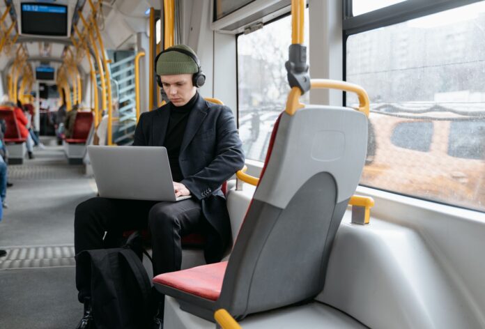 Mężczyzna w czarnym płaszczu pracuje na laptopie w tramwaju Mężczyzna w czarnym płaszczu pracuje na laptopie w tramwaju