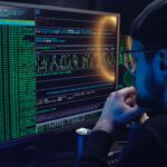 Pracownik analizuje kod na dwóch monitorach w ciemnym biurze