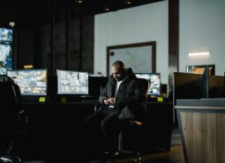 Pracownik ochrony w ciemnej dyżurce obserwuje firmowe monitory monitoringu